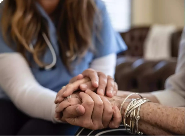 woman in scrubs holding the hand of an elderly person