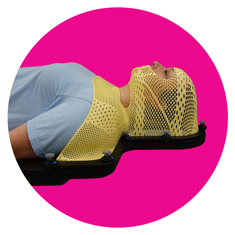 Patient lying on couchtop wearing yellow thermoplastic mask with open neck and open face