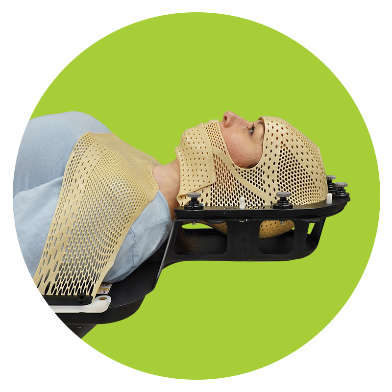Patient lying on couchtop wearing yellow head, neck, and shoulder thermplastic mask for SRS treatment