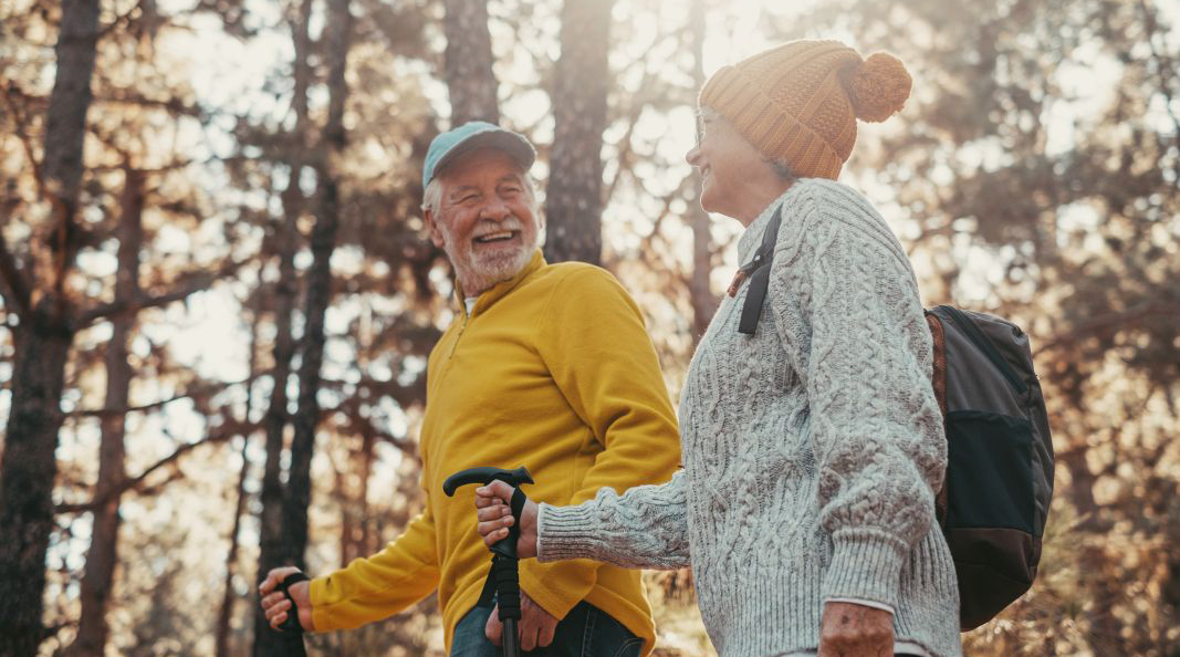 older man and woman looking happy while hiking in the woods